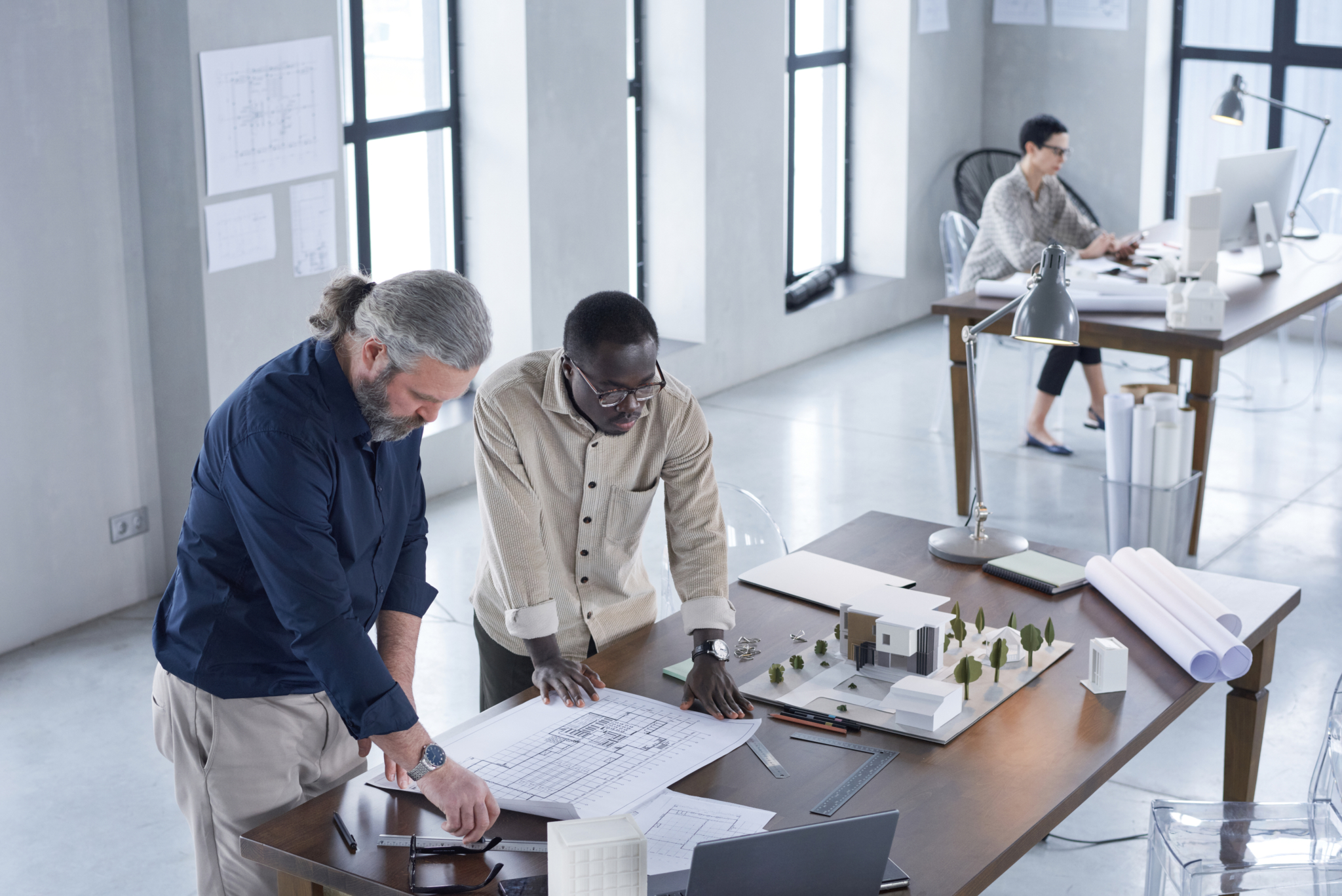 A group of colleague collaborate over a co-working table adorned with papers displaying data, a laptop and tablet device.